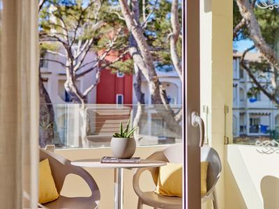 Balkon se dvěma židlemi, malým stolkem a rostlinou s výhledem na slunné nádvoří.