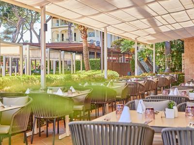 Covered outdoor restaurant area with set tables and green chairs in daylight.