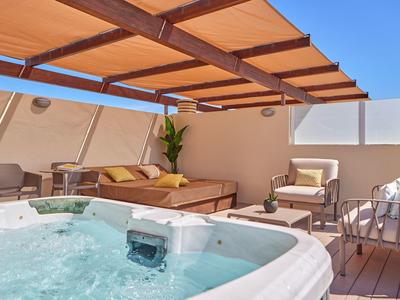 Moderní venkovní prostor s vířivkou, lounge nábytkem a stíněním pod modrou oblohou.