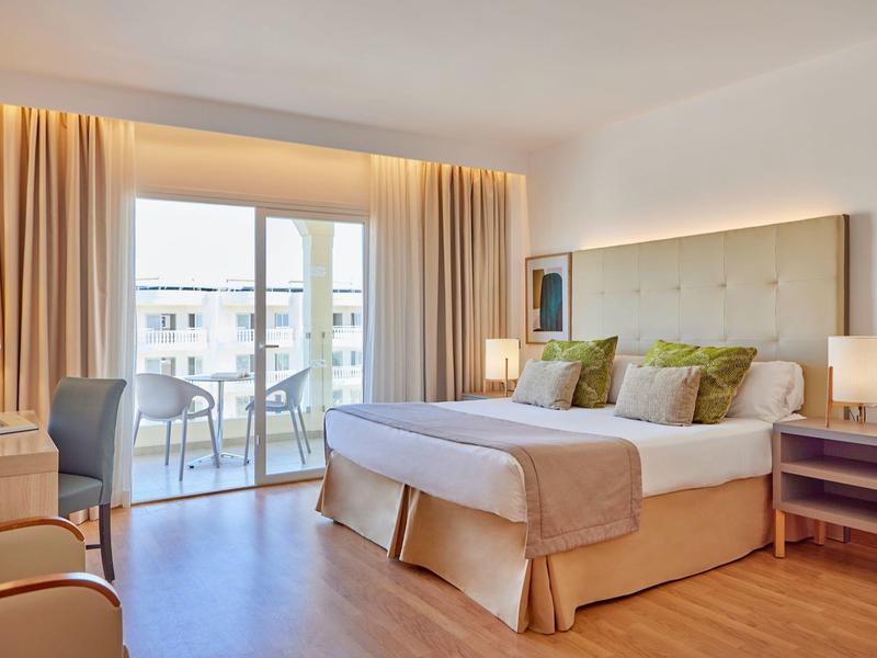 Světý hotelový pokoj s manželskou postelí, balkonem a moderním zařízením.