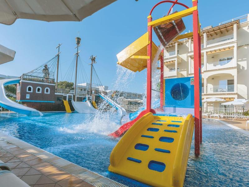 Barevné vodní hřiště s tobogány a lodí v bazénu před hotelem.
