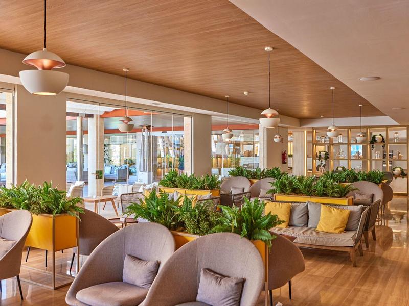 Moderní hotelový salonek s pohodlnými křesly, rostlinami a dřevěnými prvky.