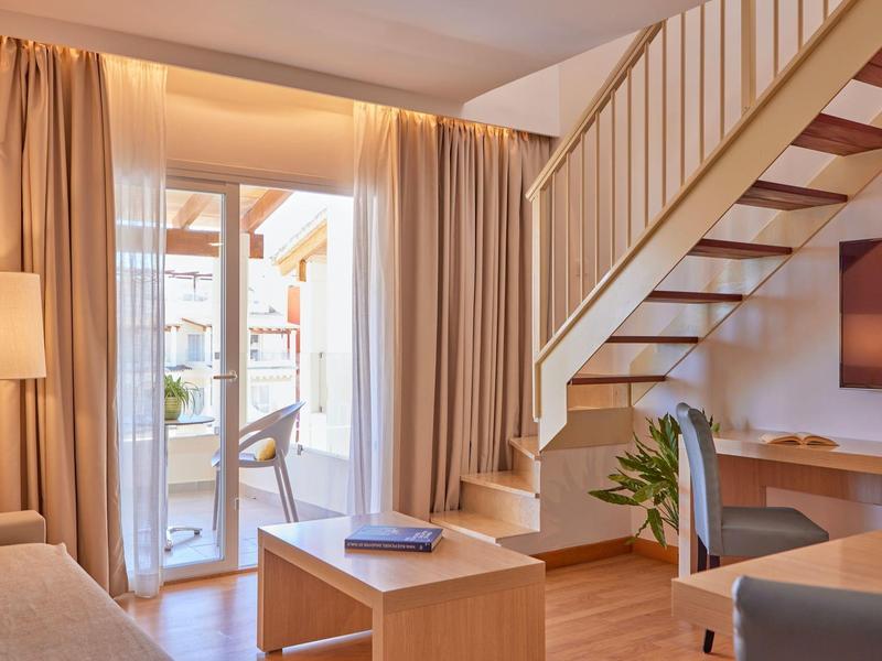 Světý obývací pokoj s točitým schodištěm, závěsy, pohovkou a TV v hotelovém pokoji