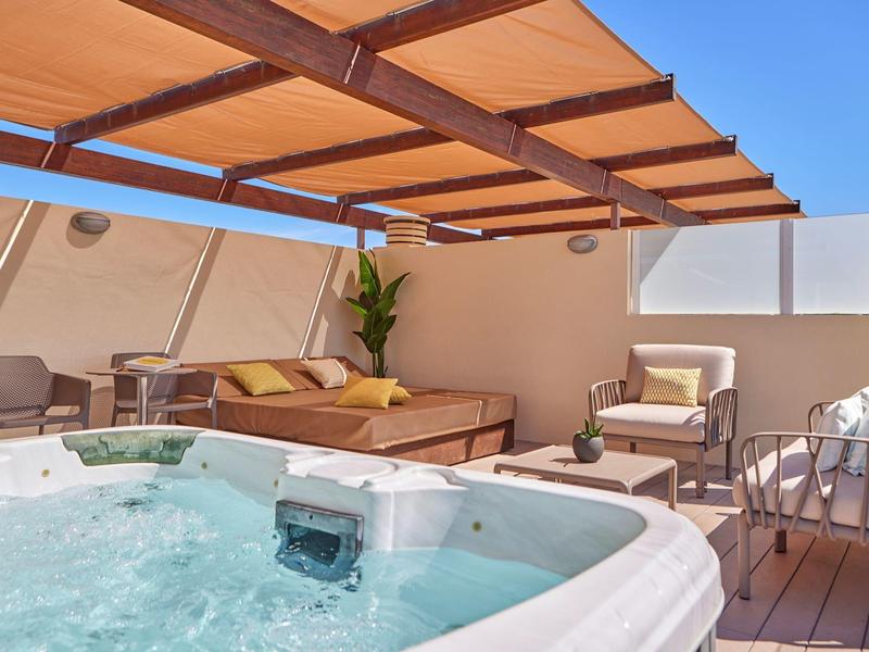 Moderní venkovní prostor s vířivkou, lounge nábytkem a stíněním pod modrou oblohou.