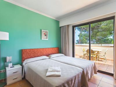 Lichte hotelkamer met twee eenpersoonsbedden, groene muur en balkon met zithoek.