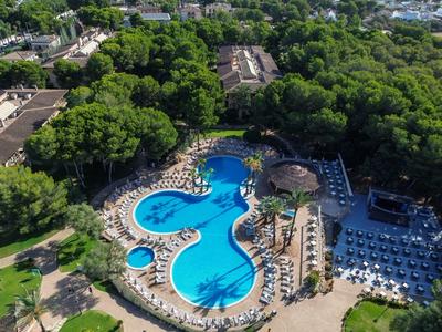 Großer blauer Pool in organischer Form, umgeben von Sonnenschirmen, Liegestühlen und viel grünem Laub.