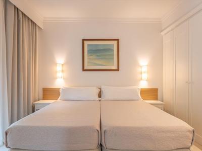Habitación de hotel luminosa con dos camas individuales, mesitas de noche y un cuadro abstracto en la pared.