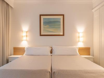 Habitación de hotel luminosa con dos camas individuales, muebles de madera y luz suave.