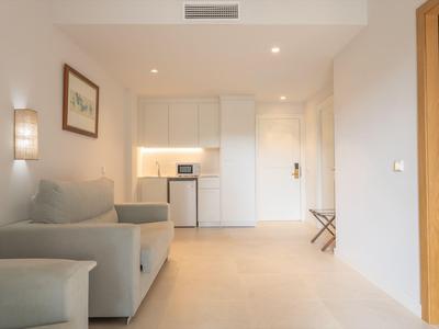 Helles Hotelzimmer mit Sofa, Minikühlschrank und Küchenzeile in neutralen Farben.