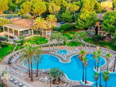 Hotelpool mit ungewöhnlicher Form, umgeben von Palmen und Liegestühlen in einer grünen Anlage.