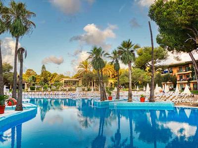 Großer Hotelpool mit Palmen und Liegestühlen unter blauem Himmel.
