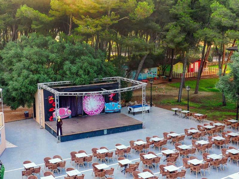 Escenario al aire libre con muchas sillas frente a una terraza rodeada de árboles en un hotel.