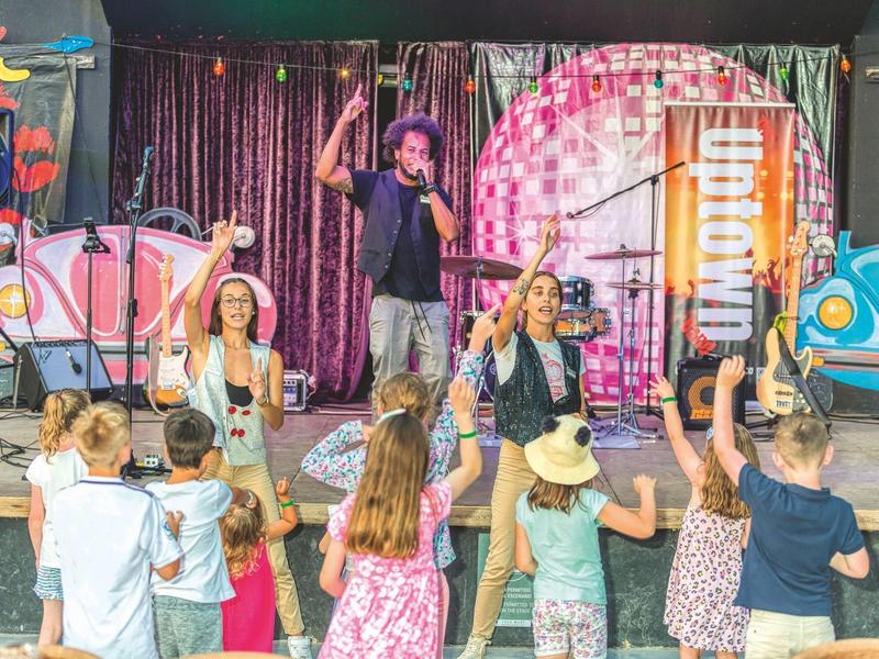 Niños bailan frente a un escenario con músicos en un entorno decorado y colorido.