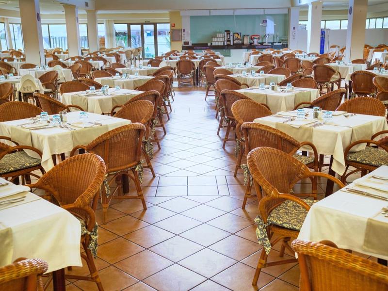 Amplio comedor con muchas mesas puestas y sillas de mimbre, interior luminoso.