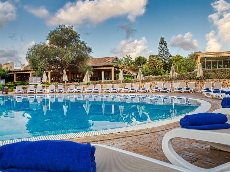 Piscina redonda del hotel con toallas azules y tumbonas bajo un cielo azul.