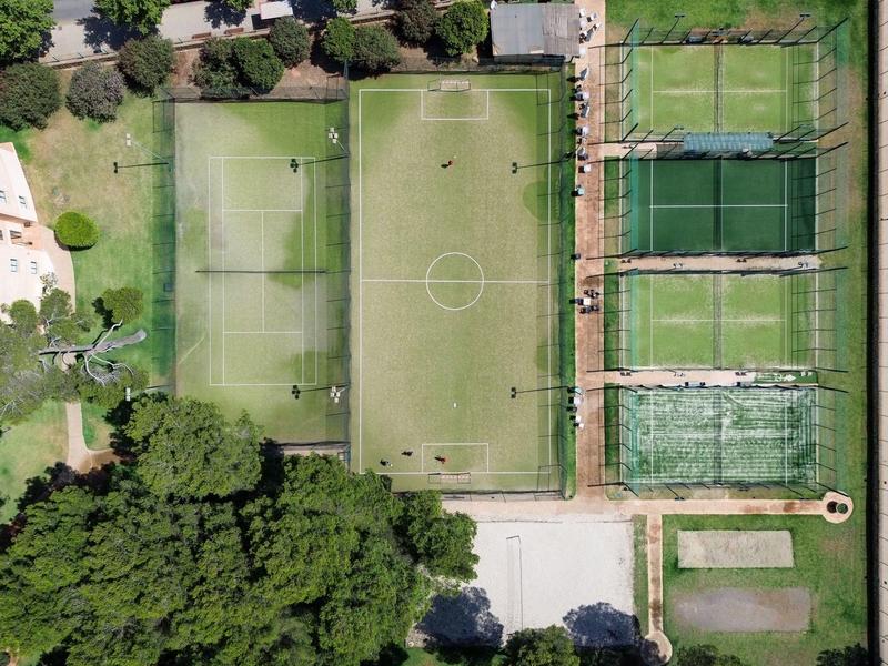 Vista aérea de canchas deportivas cercadas, incluyendo un campo de fútbol y varias pistas de tenis.
