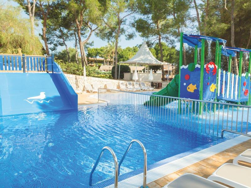 Área de piscina para niños con tobogán de agua y juegos en el jardín del hotel.