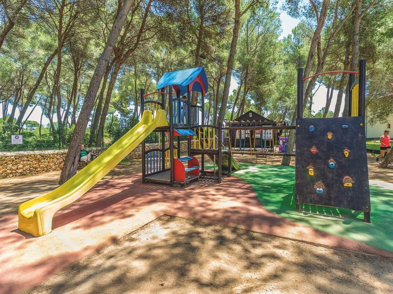 Área de juegos con tobogán y muro de escalada en una zona boscosa de recreo.