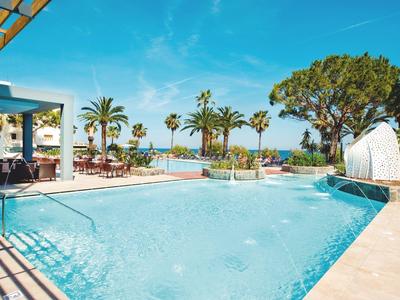 Duży basen na świeżym powietrzu z tarasem i palmami, widok na morze pod błękitnym niebem.