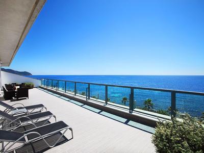 Balkon z leżakami i szklaną balustradą z widokiem na morze pod błękitnym niebem.