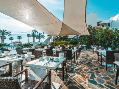 Area esterna di un ristorante con tavoli, sedie e tende da sole.