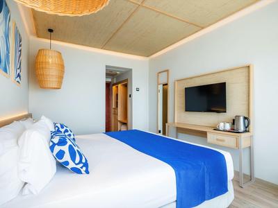 Modernes Schlafzimmer mit großem Bett, blauer Bettdecke, Flachbildschirm und hellem Holzmöbel.