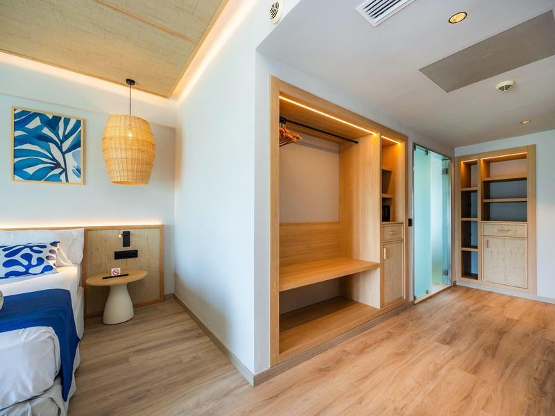 Nowoczesny pokój hotelowy z drewnianą podłogą, otwartą szafą i niebiesko-białym łóżkiem.