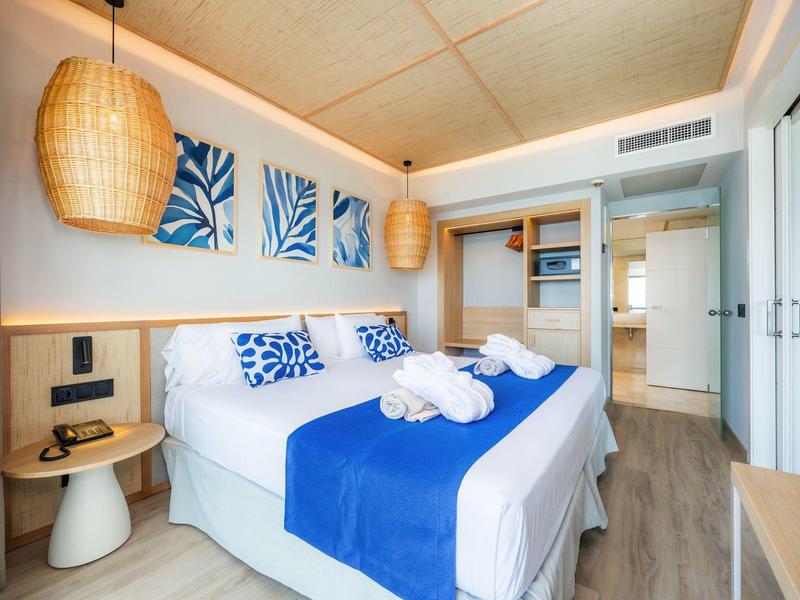 Nowoczesny pokój hotelowy z podwójnym łóżkiem, niebieskimi akcentami i dekoracjami ściennymi.