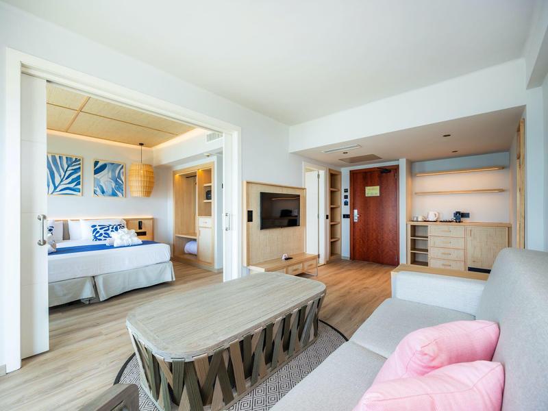 Jasny pokój hotelowy z częścią wypoczynkową, otwartą sypialnią i nowoczesnym wystrojem.