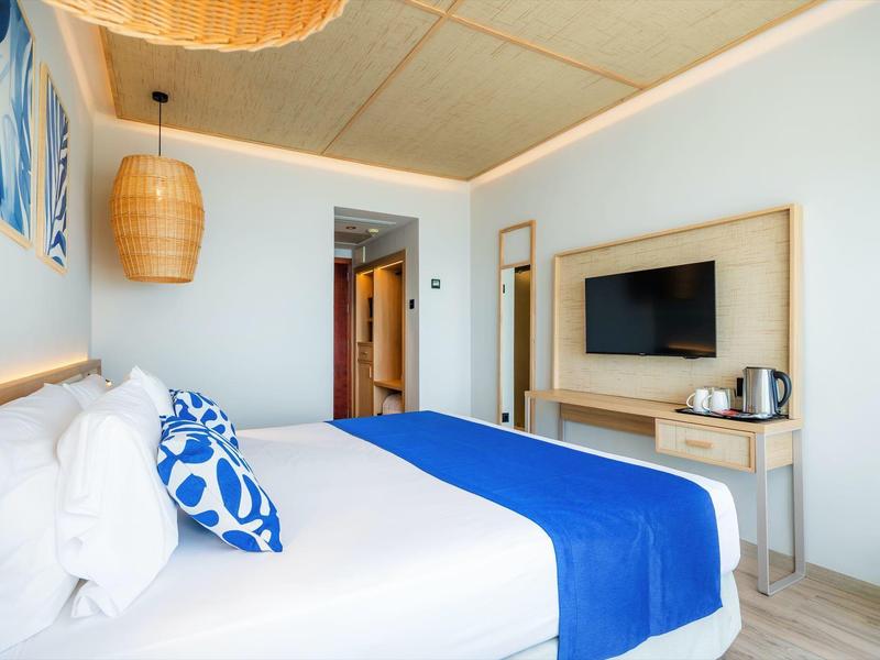 Nowoczesny pokój hotelowy z dużym łóżkiem, niebieską narzutą i telewizorem na ścianie.