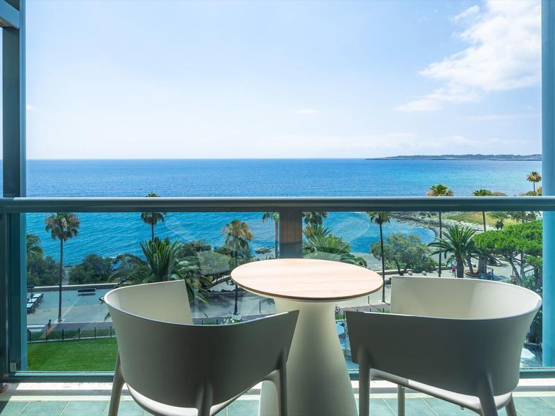 Balkon z stołem i krzesłami z widokiem na morze w słoneczny dzień.