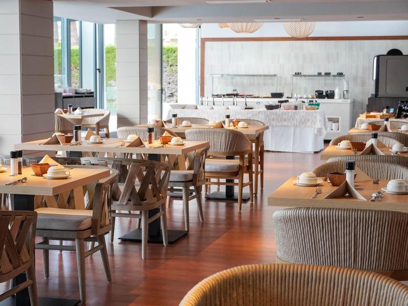 Jasna restauracja z nowoczesnymi drewnianymi meblami i nakrytymi stołami przy dużych oknach.