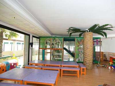 Wewnętrzny plac zabaw dla dzieci z kolorowymi konstrukcjami, stołami i palmą.