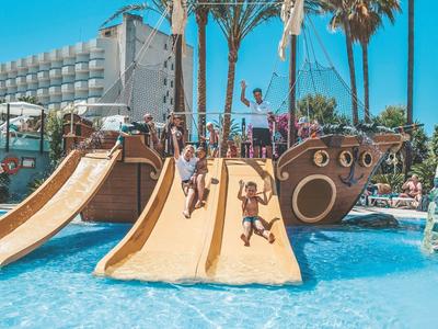 Dzieci bawią się na zjeżdżalniach w kształcie statku pirackiego w basenie hotelowym pod palmami.