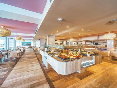 Przestronna część bufetu z drewnianą podłogą, białymi ladami i licznymi miejscami do siedzenia, różowe ściany.