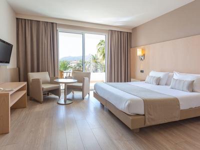 Modernes Hotelzimmer mit großem Bett, Sofa, Tisch, TV und Balkon mit Meerblick.