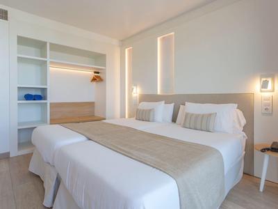 Helles Schlafzimmer mit Doppelbett, offener Garderobe und warmem LED-Licht an weißen Wänden.
