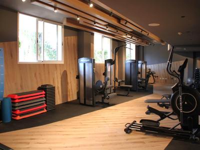 Moderner Fitnessraum mit Holzfußboden, Trainingsgeräten und drei großen Fenstern an der Wand.