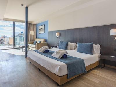 Modernes Hotelzimmer mit großem Doppelbett, blauen Akzenten und Panoramafenster zur Terrasse.