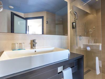 Moderne Badezimmer mit großem Spiegel, rechteckigem weißen Waschbecken und Glastür zur Dusche.