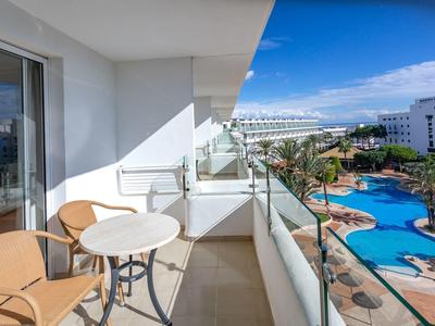 Balkon z stołem i krzesłami z widokiem na basen i hotele w słoneczny dzień.