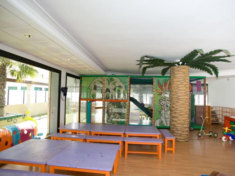 Wewnętrzny plac zabaw dla dzieci z kolorowymi konstrukcjami, stołami i palmą.