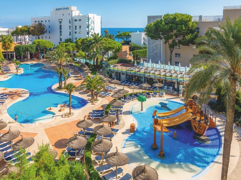 Basen w ośrodku z leżakami, palmami, parasolami i zjeżdżalnią wodną blisko morza.