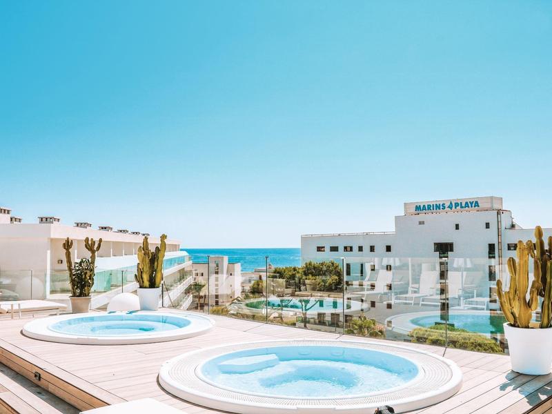 Taras na dachu z dwoma jacuzzi, kaktusami, budynkami i widokiem na morze pod czystym niebem.