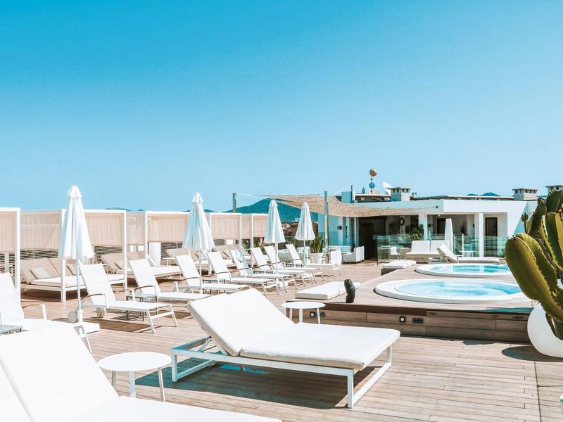 Słoneczny taras na dachu z białymi leżakami i okrągłymi basenami pod bezchmurnym niebem