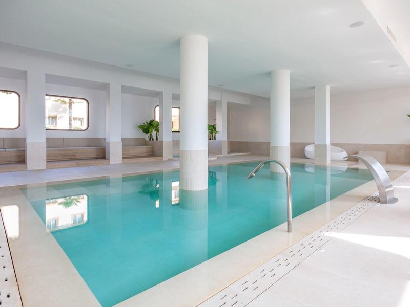 Kryty basen hotelowy z białymi ścianami, kolumnami i naturalnym światłem z okien.