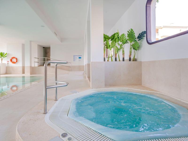 Wewnętrzna strefa spa z bulgoczącym jacuzzi i basenem w tle.