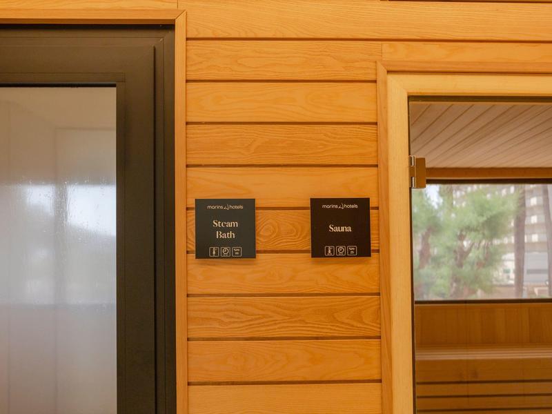 Korytarz hotelowy z drewnianymi panelami, windami i oznaczeniami pokoi