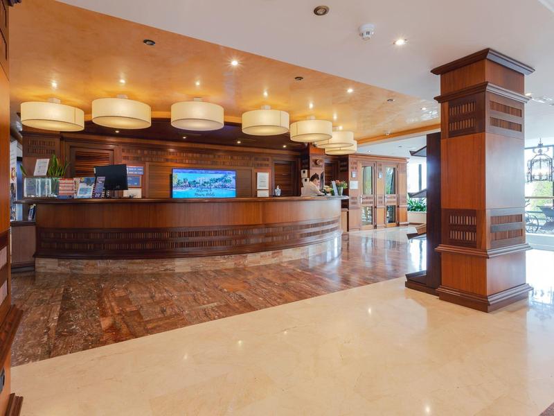 Przestronny hol recepcyjny hotelu z drewnianymi ladami, ciepłym oświetleniem i marmurowymi podłogami.