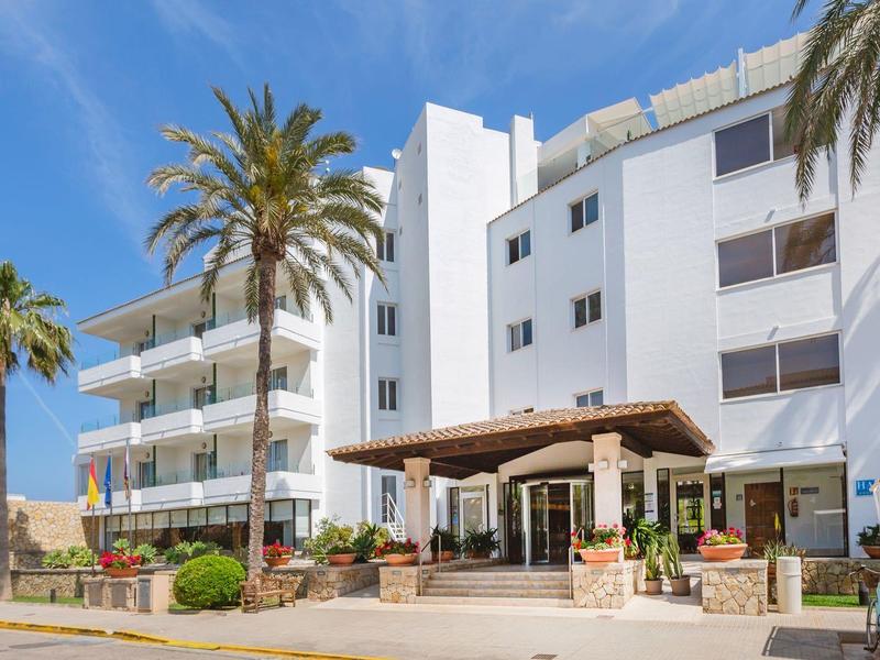 Biały budynek hotelowy z balkonami i palmami pod bezchmurnym niebem.